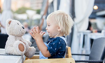 Kind_sitzt_im_Hochstuhl_mit_Kuscheltier