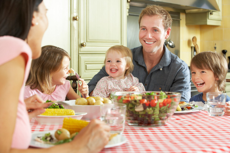 Familie_mit_drei_Kindern_sitzt_am_Essenstisch_mit_gesunden_Lebensmitteln